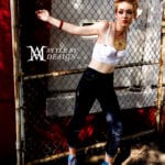 A young woman leans against a chain-link fence in casual attire.