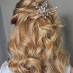 Blonde hair styled in loose curls with a decorative hairpiece.