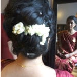 A woman with flowers in her braided hair looking in a mirror.