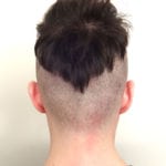 Back view of a person's head with an unusual haircut, shaved sides, and a patch of hair at the top.