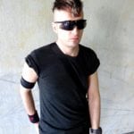 A man wearing sunglasses and a black outfit with arm accessories.