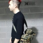Side view of a man with a red mohawk and camouflage backpack.