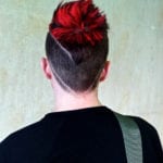 Back view of a person with a creative undercut hairstyle featuring a red bun and shaved geometric design.