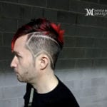 Side profile of a man with a unique red mohawk and shaved patterns.