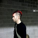A man with a red mohawk hairstyle standing against a brick wall.