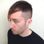 Side profile of a man with a short, modern haircut wearing a black shirt.