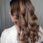 Curly brown hair with soft highlights on a person wearing a white shirt with yellow dots.
