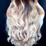 Long wavy blonde hair with dark roots.