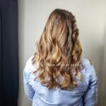 A woman with long wavy hair wearing a light blue shirt, seen from behind.