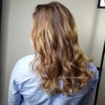 Back view of a woman with long, wavy blonde hair.