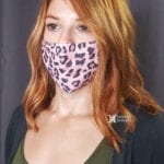 A woman with red hair wearing a pink leopard print face mask.