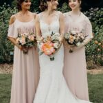 Bride in white dress with two bridesmaids in blush gowns holding bouquets.