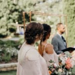 Bride and groom exchanging vows outdoors with bridesmaid close by.