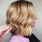 Side profile of a woman with wavy blonde hair and a hand adjusting the strands.