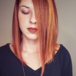 A woman with straight, shoulder-length red hair covering one eye.