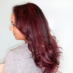 Profile of a woman with long burgundy hair wearing a gray top.