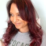A woman with long reddish hair smiling gently, wearing a gray shirt.