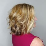 Profile of a woman with short, wavy blonde hair wearing a pink top.