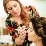 A makeup artist applying eye makeup to a seated woman.