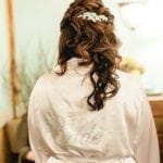 A woman with wavy hair wearing a white robe with 'Bride' embroidered on the back.