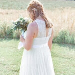 Bride in white dress holding bouquet outdoors.