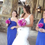 Bride in white dress with two bridesmaids in blue dresses holding pink bouquets.
