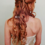 Red-haired woman with long curly hair styled in a half-updo.