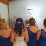 Four women in formal dresses standing with their backs to the camera.