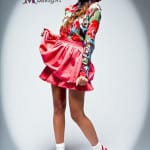 A girl in a colorful floral top and red skirt posing with sneakers.
