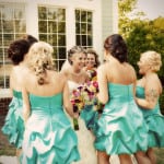 Bride and bridesmaids in turquoise dresses share a joyful moment outdoors.