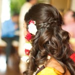 A woman with long, curled hair adorned with red and white flowers.
