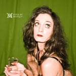 A woman with curly hair holding a glass against a green background.