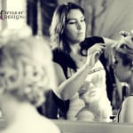 A woman styling hair in front of a mirror.