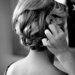 Black and white photo of a hand styling a woman's updo hairstyle.
