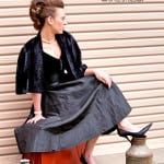 A woman in a black outfit sitting on an orange suitcase.