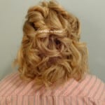 Curly blonde hair styled with a decorative clip on a person wearing a pink striped shirt.