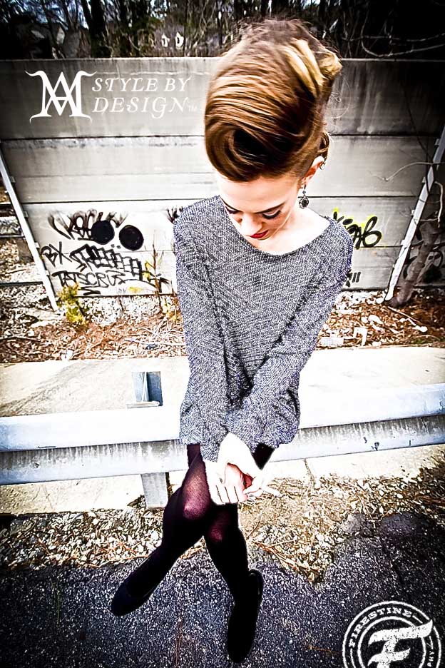 Young woman in a gray sweater looking down outdoors.