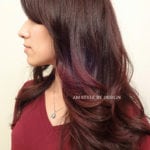 A woman with long, dark brown hair styled in loose waves with subtle purple highlights.