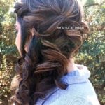 A woman with curly brown hair styled in a half-updo outdoors.