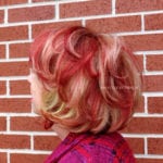 A short red and blonde hairstyle against a brick wall.