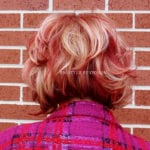 Back view of a person with short, wavy red hair wearing a pink plaid jacket.