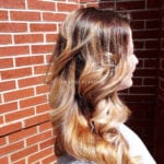 Profile of a woman with long, curled hair against a brick wall.