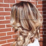 Blonde hair styled in loose curls against a brick wall.