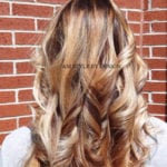 Person with long, wavy blonde hair standing in front of a brick wall.