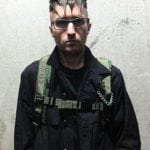 A man wearing glasses and a green harness on a black jacket.