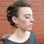 Profile of a woman with styled hair against a brick wall.