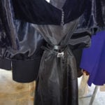 A black leather trench coat with a belt on display.