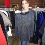 Woman holding a sparkly black sweater in a clothing store.