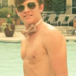 A young man in sunglasses and a bow tie by a pool.