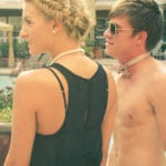 A woman in a black dress and a shirtless man with sunglasses and a bow tie.